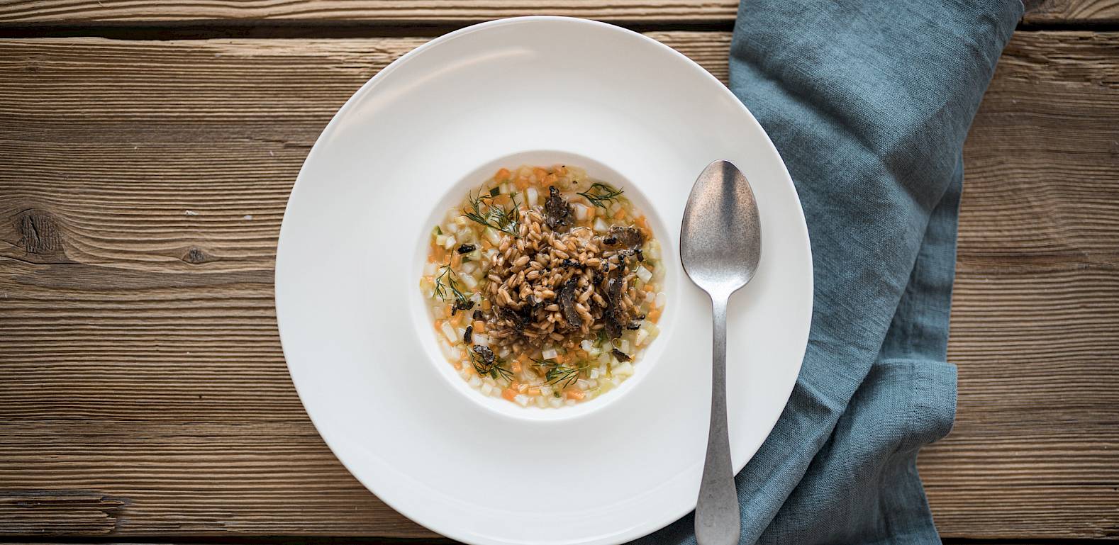 Eine Schüssel mit leckerem Müsli auf Holztisch, daneben ein Löffel und eine blaue Serviette.