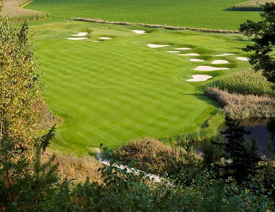 Ein gepflegter Golfplatz mit mehreren Sandbunkern, umgeben von Feldern und Bäumen in einer ländlichen Gegend.
