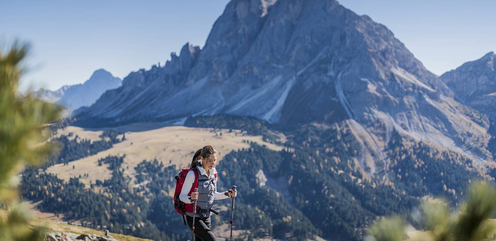 Eine Person wandert in den Alpen, mit einem beeindruckenden Berg im Hintergrund unter klarem Himmel.