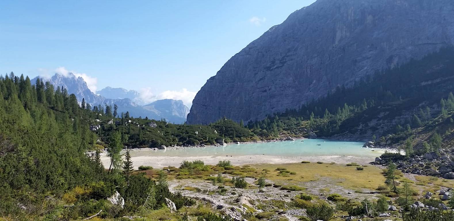 Un lago alpino con acqua turchese, circondato da foreste verdi e ripide pareti di montagna sotto un cielo sereno.
