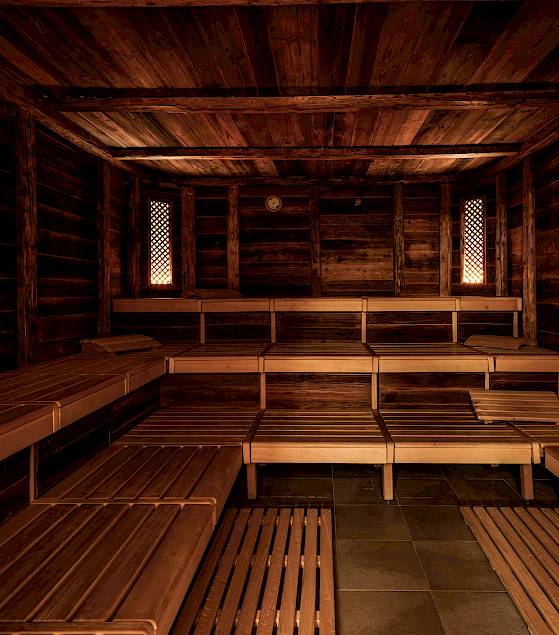 Holzvertäfelte Sauna mit Bänken, sanft beleuchtet. Einladend und bereit für Entspannung.