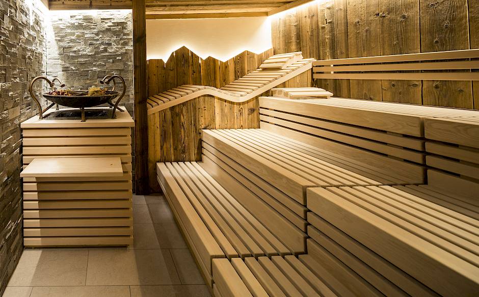 Sauna mit hölzernen Sitzbänken und rustikaler Wandverkleidung, harmonisch beleuchtet für entspannende Atmosphäre.