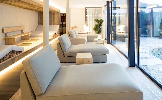 Moderne Lounge mit Liegestühlen und großen Fenstern, die auf einen steinernen Innenhof blicken. Wärme und Eleganz.