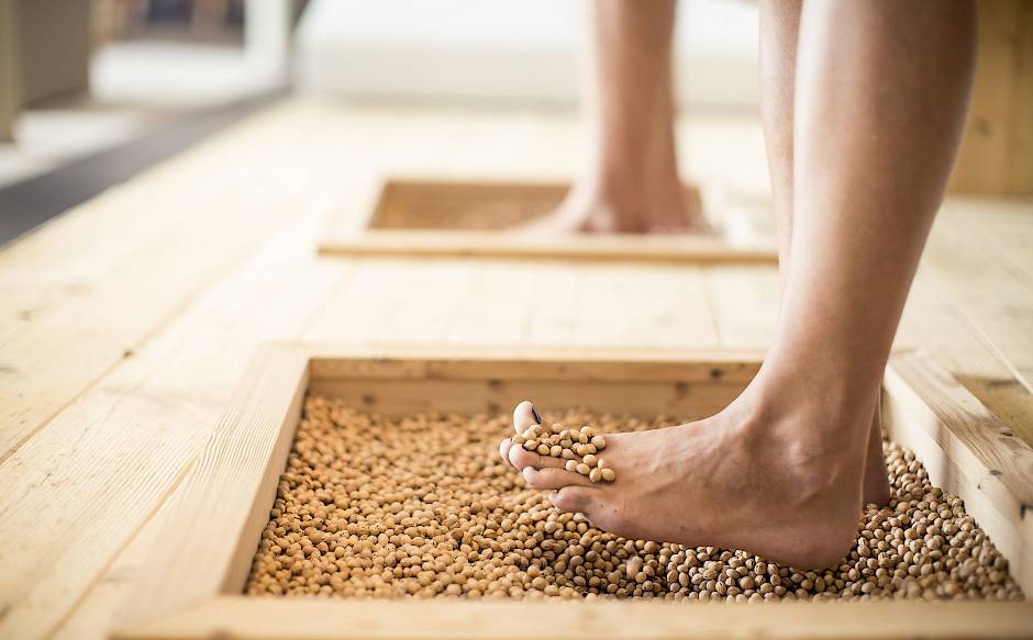 Zwei Füße treten auf Holzrahmen, gefüllt mit runden Steinen, für eine Fußmassage.