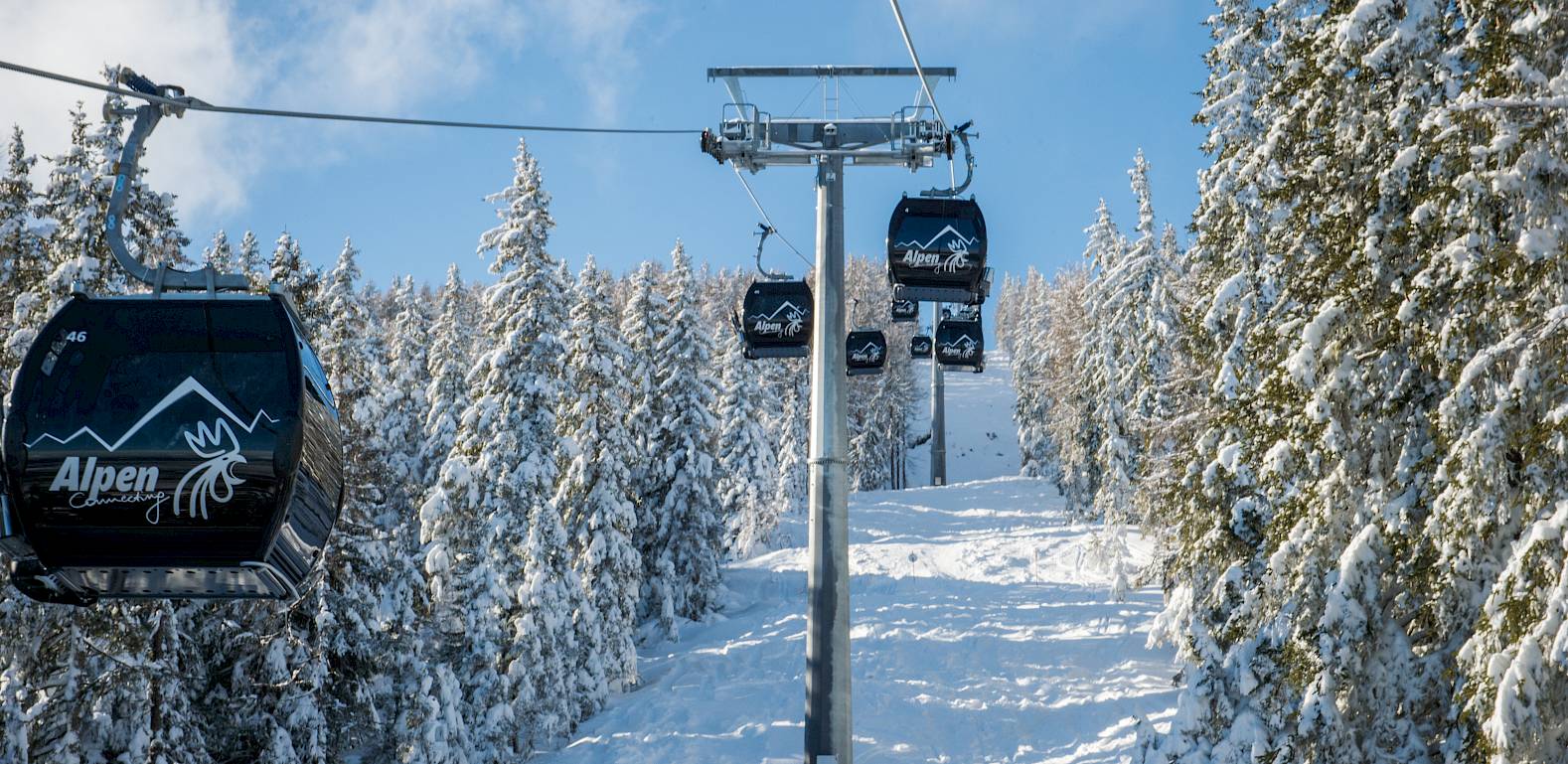 Seilbahn mit schneebedeckten Bäumen im Hintergrund, blauer Himmel über einer alpinen Winterlandschaft.