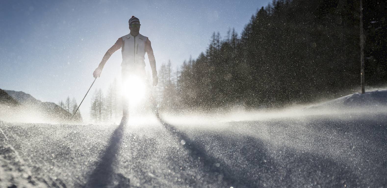 Silhouette eines Langläufers im Schnee bei starkem Sonnenlicht, das von hinten scheint.