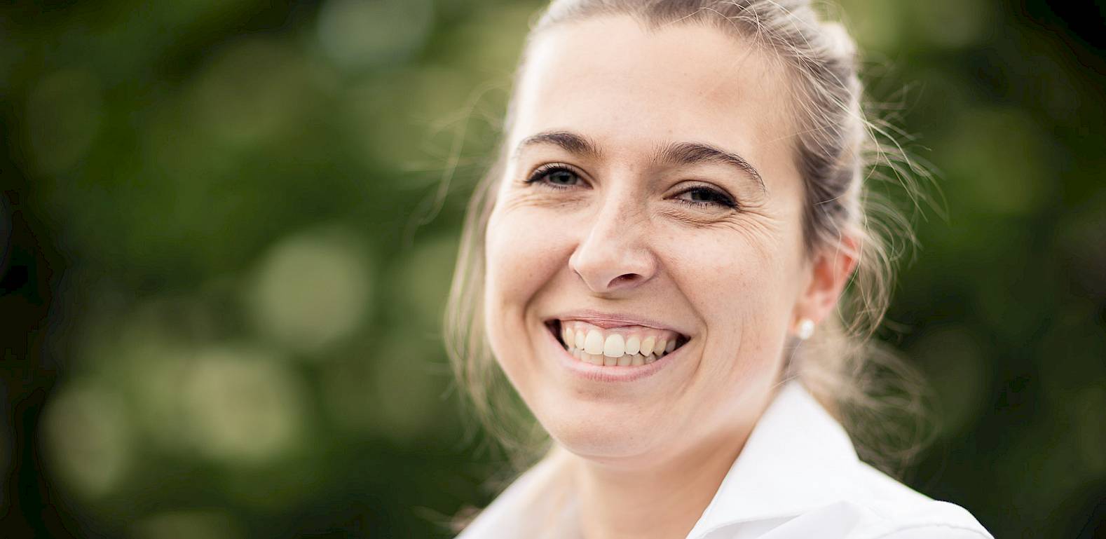 Donna con un viso sorridente e colletto bianco, davanti a uno sfondo verde sfocato.