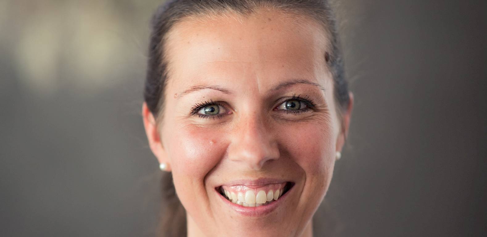 Una donna sorridente con capelli scuri e maglia nera su sfondo sfocato.