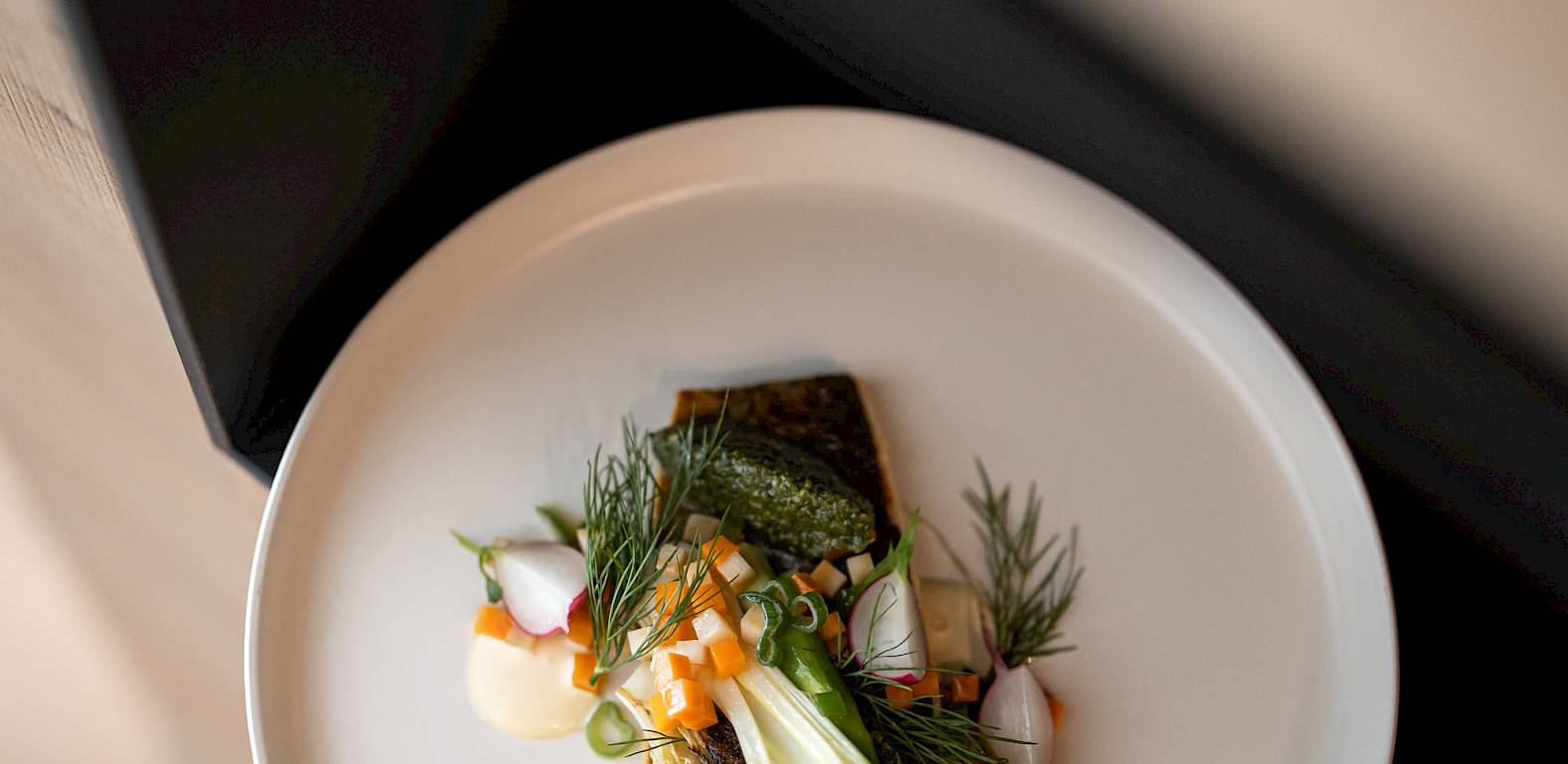 Un piatto artisticamente disposto con pesce, erbe fresche e ravanelli su un piatto bianco.