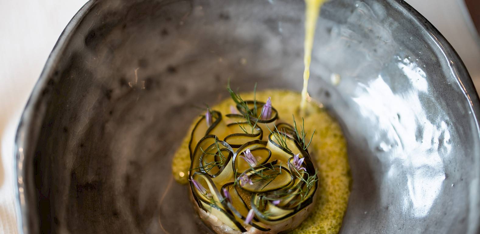 Piatto elegante con ingredienti disposti artisticamente, guarniti con salsa dorata. Decorazione da tavola bianca.