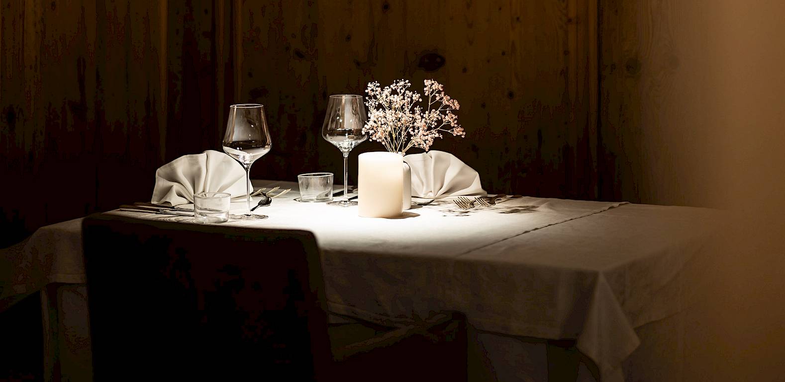 Tavolo elegante per due, apparecchiato con candela e fiori in una stanza con pannelli di legno.