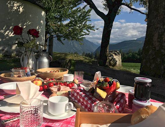 Outdoor breakfast with mountain view, sunlight casting on a table laden with food.
