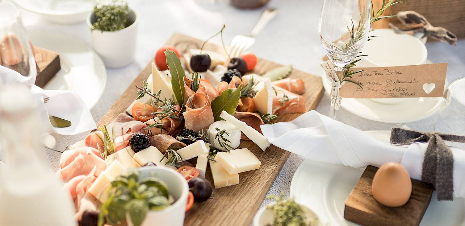 Elegant gedeckter Tisch im Freien mit Vorspeisen, Brot, Gemüse und Getränken in der Morgensonne.