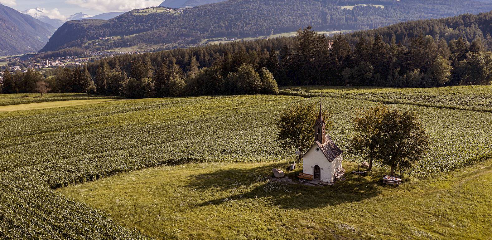 Kleine Kapelle auf einem weiten Feld mit Bergen im Hintergrund unter klarem Himmel.