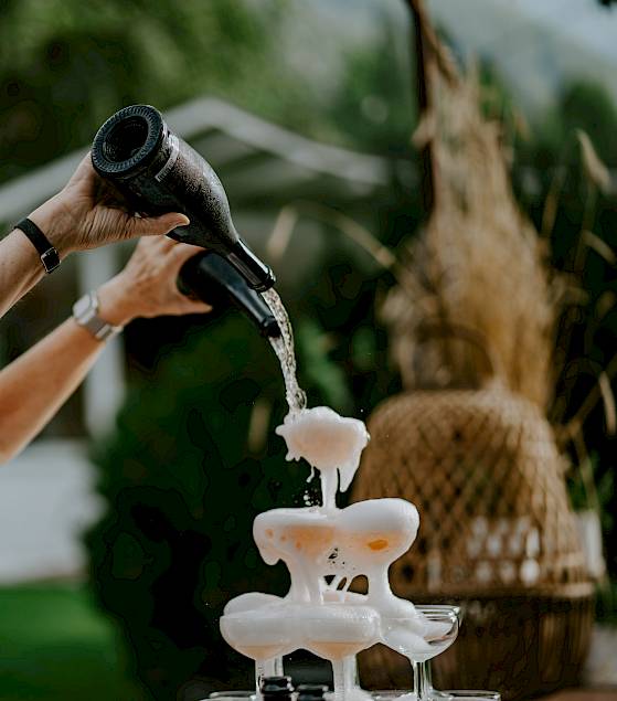 A person pours liquid from two jugs into a sculptural structure outdoors.