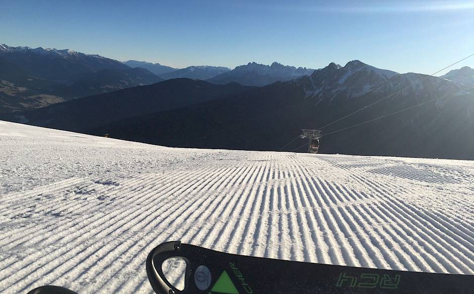 Skis on freshly groomed piste with mountain view in the early morning.