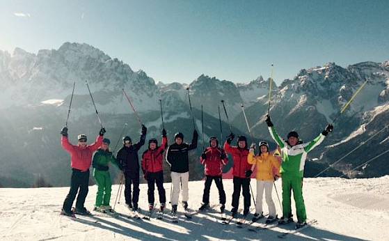A group of skiers in front of mountains joyfully lifts their ski poles. Sunny weather.