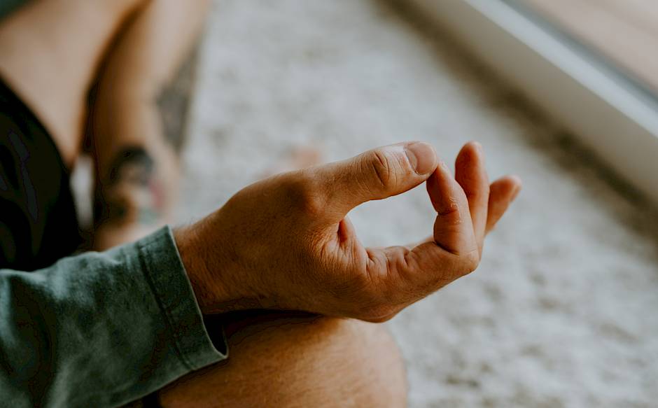 Person sitting cross-legged on the floor meditating, with focus on hand position.
