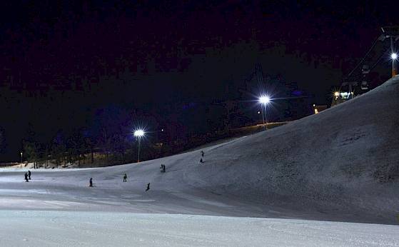 Several skiers enjoy night skiing on a lit slope, surrounded by darkness.