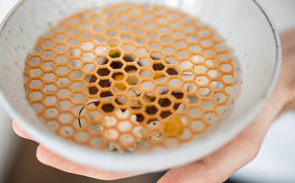 A hand holds a bowl with an artistic dessert and a caramel lattice pattern.