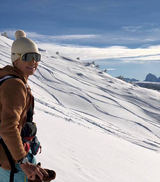 Person hiking in snowy mountains, wearing a backpack and hat. Sunny, clear sky.