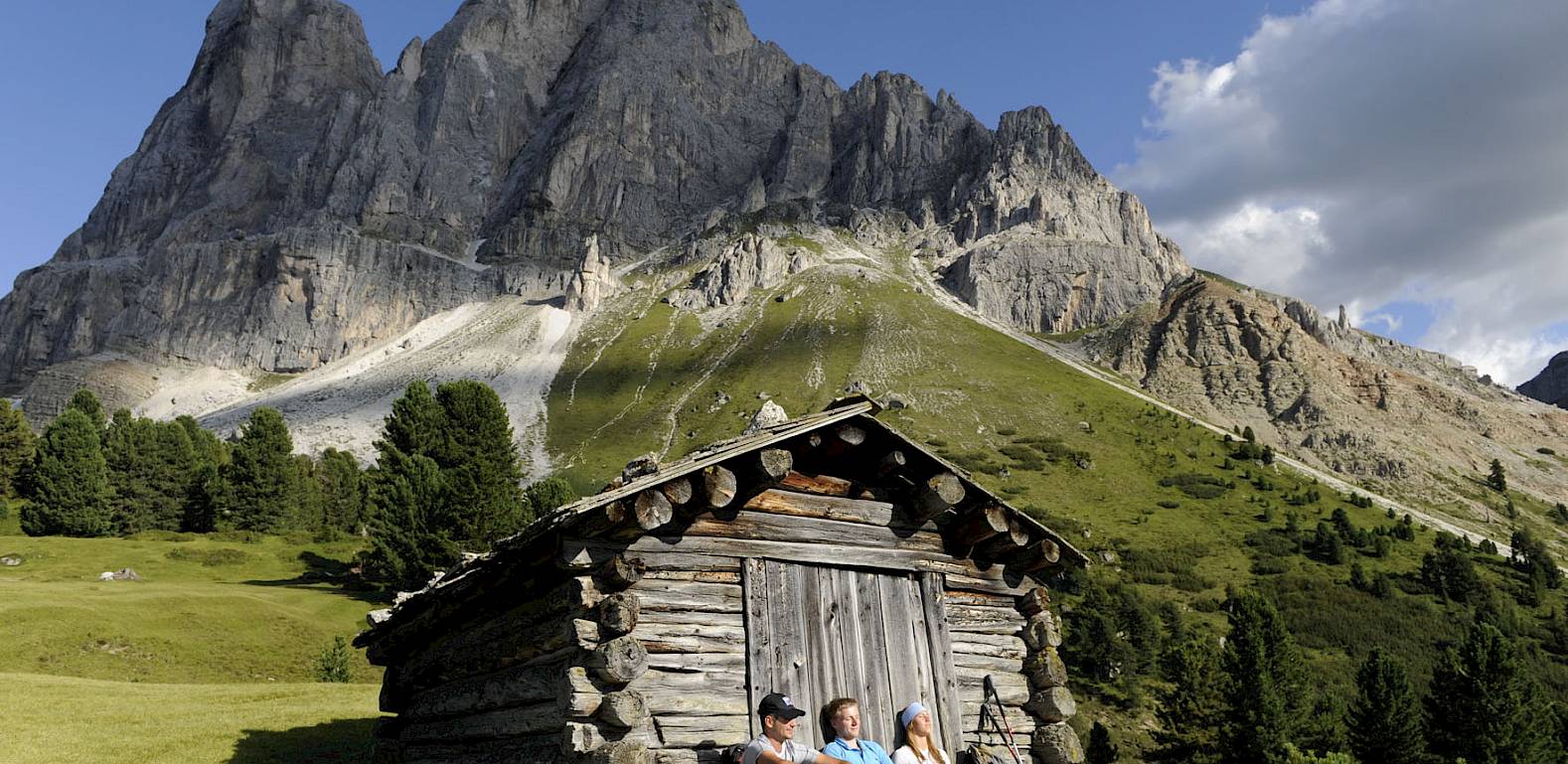 Un gruppo di persone si rilassa davanti a una baita di legno con montagne sullo sfondo.