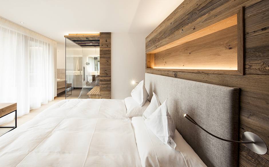 Camera da letto moderna con pareti in legno, grande letto, cuscini bianchi e luce naturale da ampie finestre.