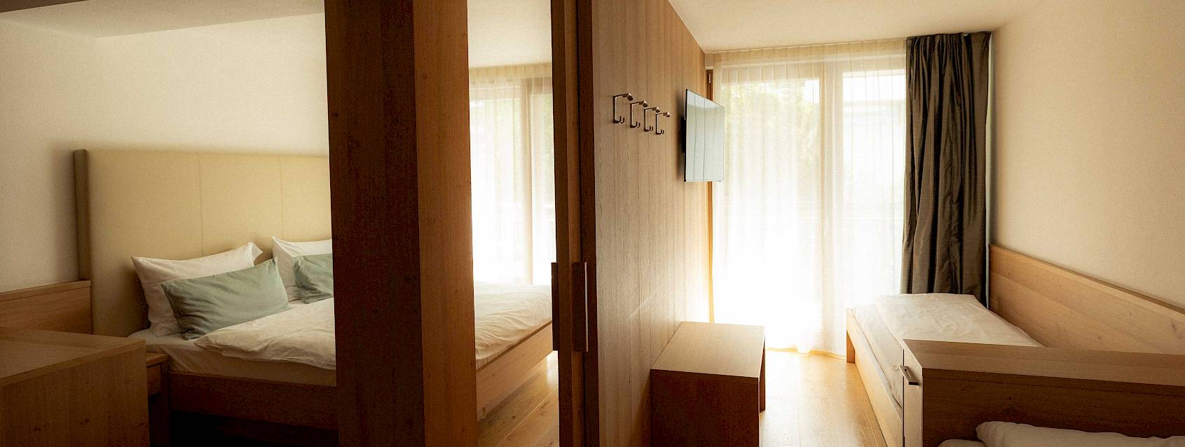 Zwei Schlafzimmer in warmen Holztönen mit Einzel- und Doppelbett, getrennt durch eine Schiebetür. Natürliches Licht.