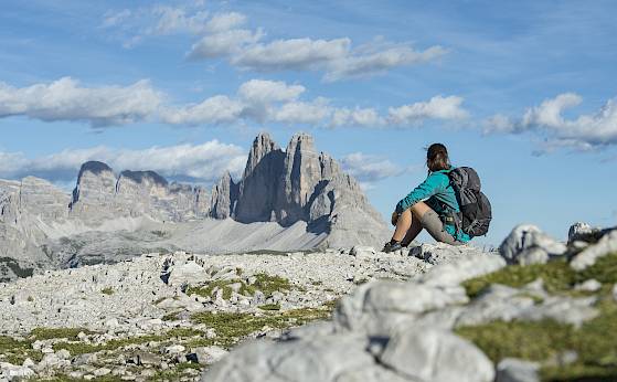 Eine Person in Wanderkleidung genießt die Aussicht auf die Drei Zinnen in den Dolomiten.