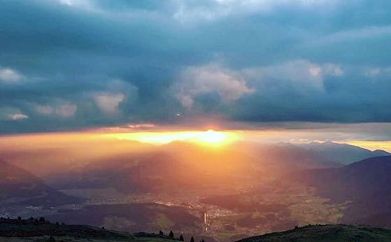 Sonnenuntergang über Bergen mit dramatischen Wolken und goldenem Licht, das sanft die Landschaft erhellt.