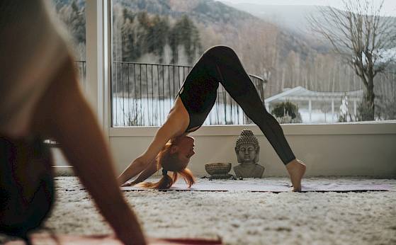 Frau macht Yoga im herabschauenden Hund in einem Raum mit Ausblick auf verschneite Berge. Zen-Atmosphäre.