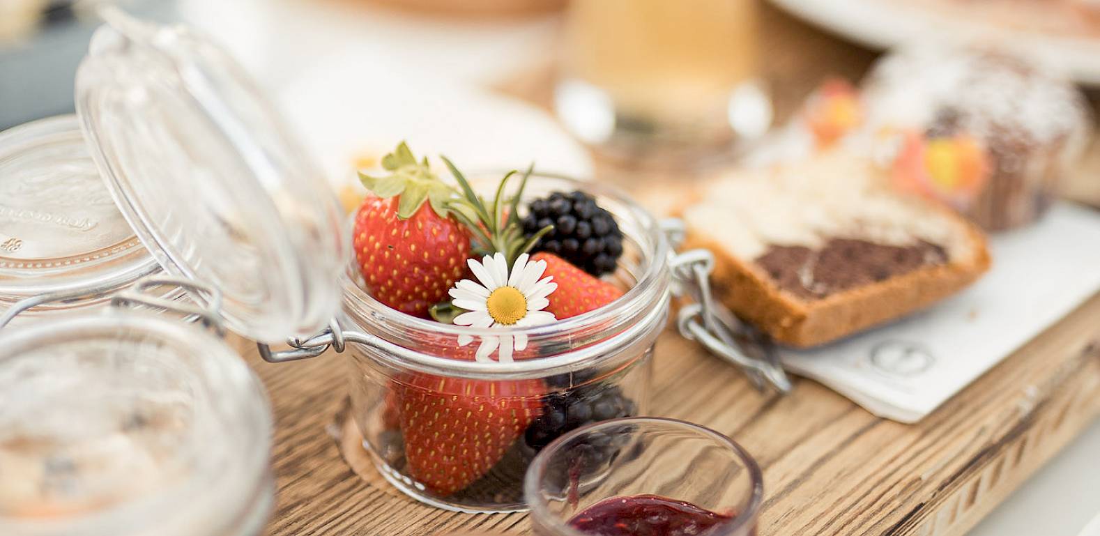 A wooden table with jam, fruit in a jar, and pastries, carefully set for breakfast.