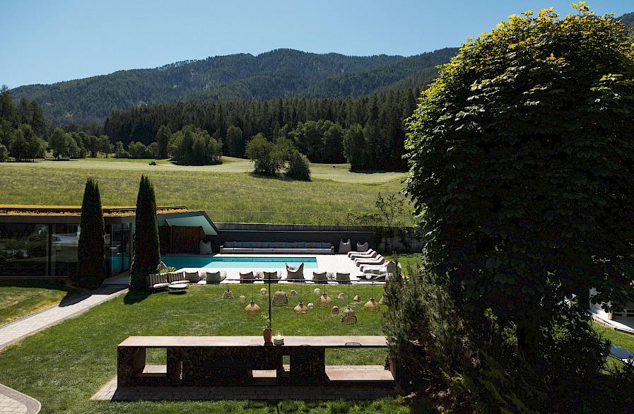 Eine moderne Außenanlage mit Pool, umgeben von grünen Wiesen und Wald, unter klarem Himmel.