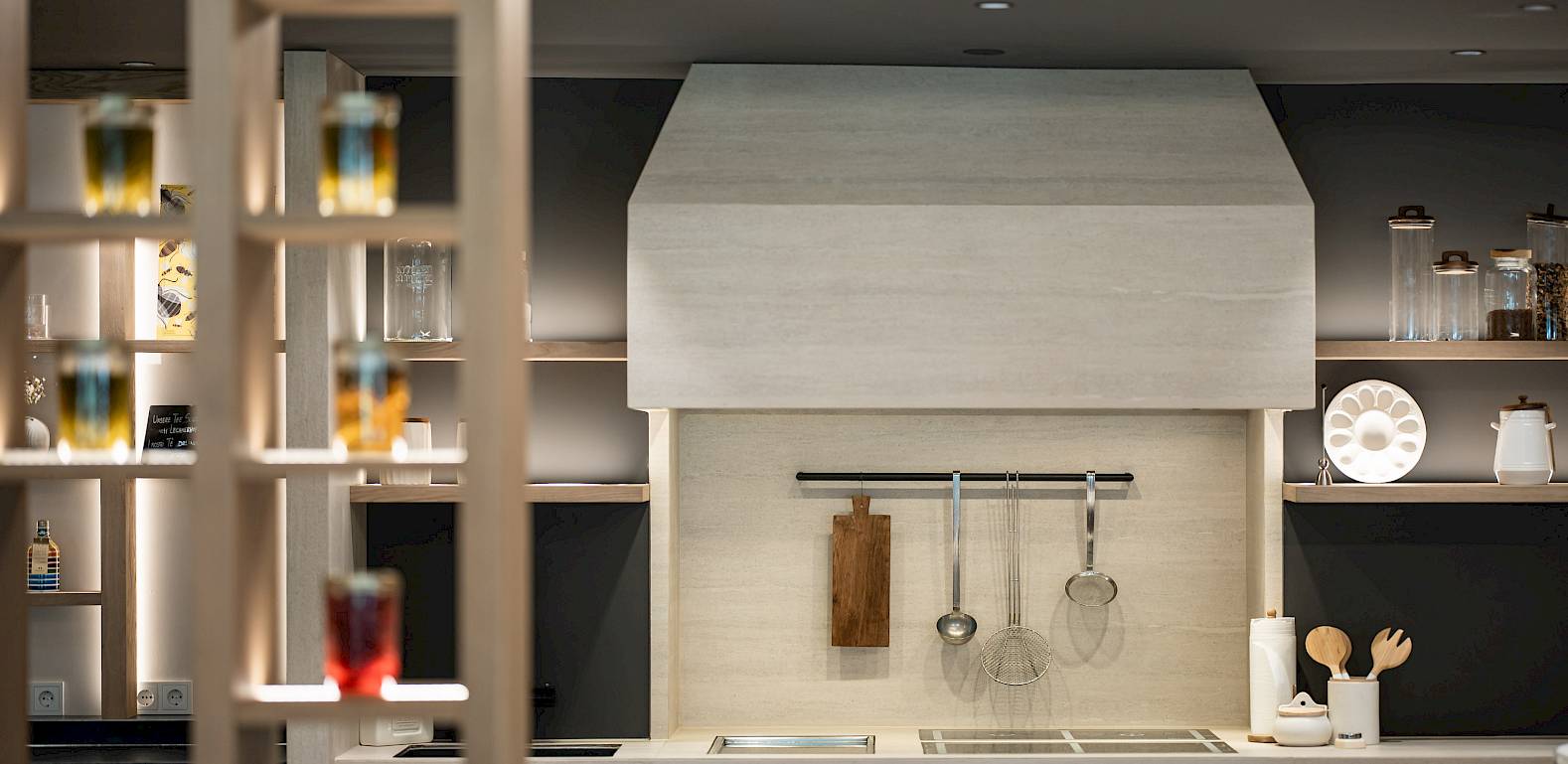 Moderne Küche mit Holzmöbeln, Küchengeräten und stilvoller Beleuchtung. Gewürzgläser im Vordergrund.