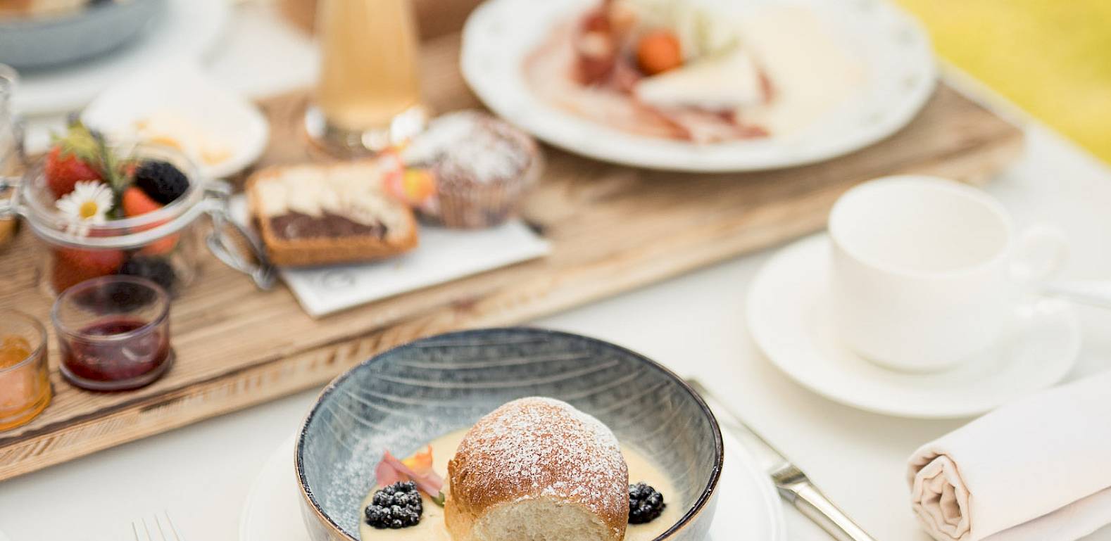 Elegantes Frühstück im Freien mit Gebäck, frischen Früchten und Aufschnitt, auf einem weiß gedeckten Tisch.