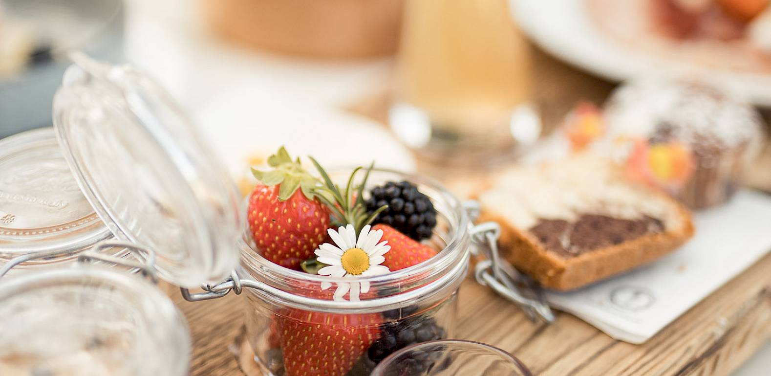 Ein rustikales Frühstückstablett mit frischen Beeren, Marmeladen und geröstetem Brot im Freien.