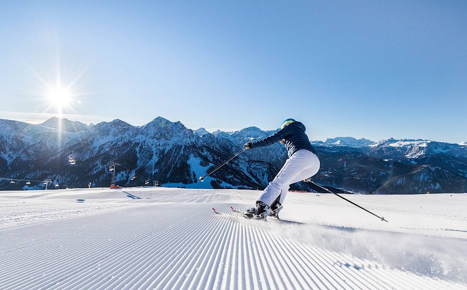 Skifahrer bei Sonnenschein auf frisch präparierter Piste mit Berglandschaft im Hintergrund.