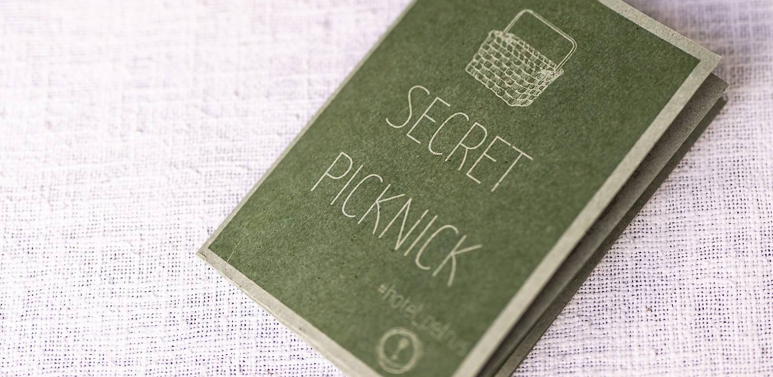 A small green notebook with "Secret Picknick" text lies on white fabric.