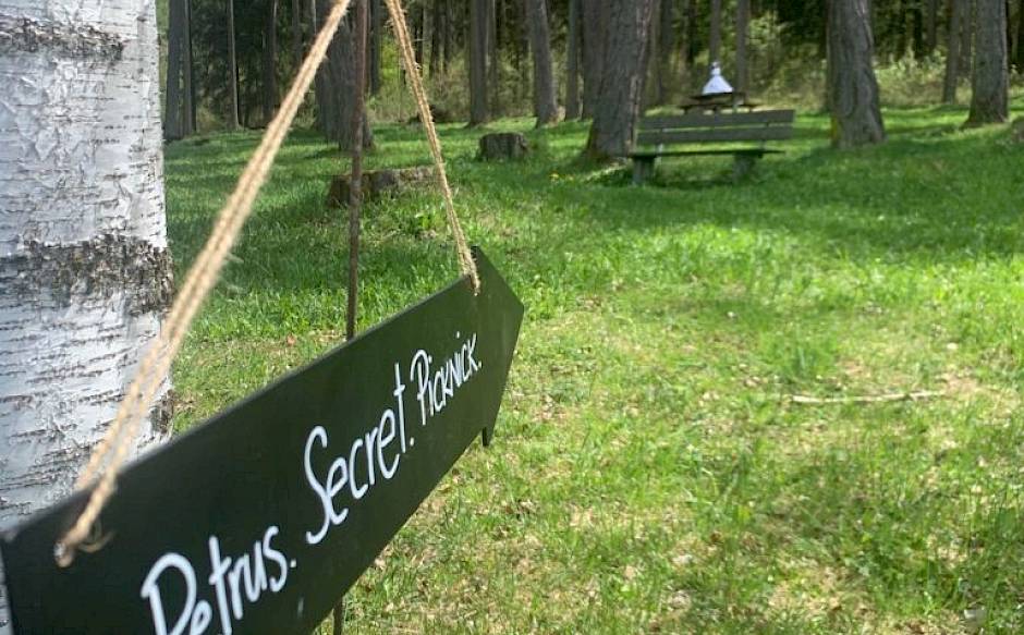 Ein Schild mit der Aufschrift "Petrus. Secret. Picnic." weist auf einen Picknickplatz im Wald hin.