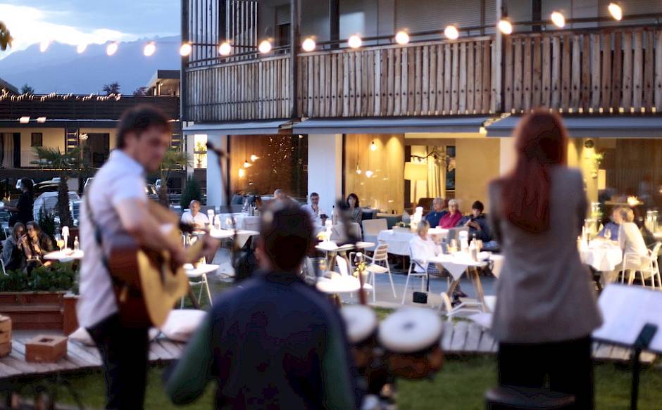Ein Musikertrio spielt im Freien vor einem stilvollen Restaurant mit Gästen bei Dämmerung.