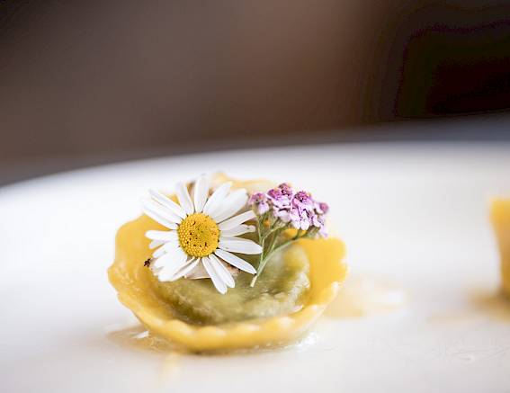 Raviolo con fiore delicato e guarnizione su piatto bianco, messa a fuoco sui dettagli.