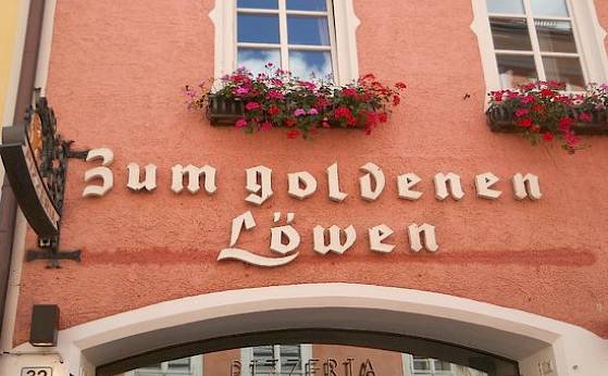 Facade of the building "Zum goldenen Löwen" with flower boxes on windows and pink wall.