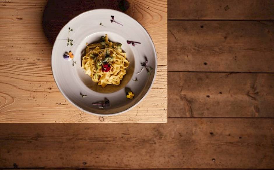 A plate of pasta, garnished with herbs and a tomato, on a wooden table. Top view.