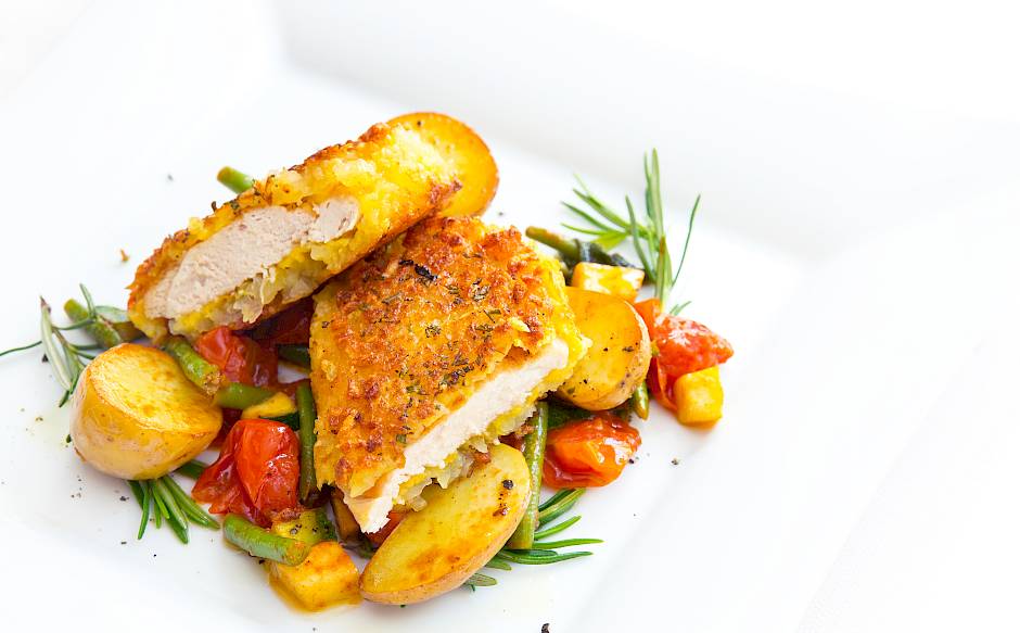 Crispy breaded chicken breast with new potatoes, tomatoes, and rosemary on a white plate.