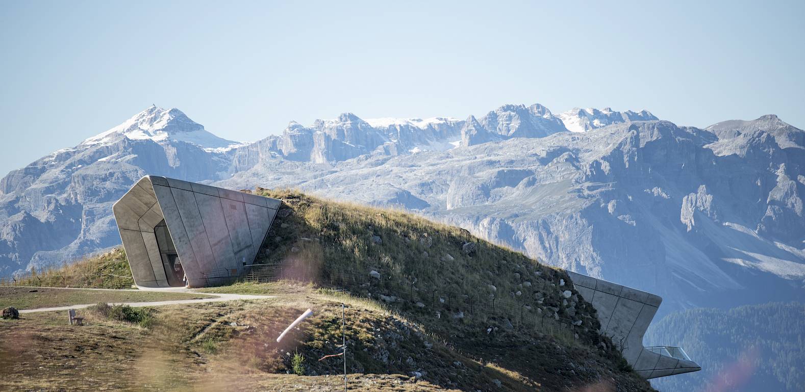 A modern building with geometric shapes stands in a mountainous landscape with snow-capped peaks.