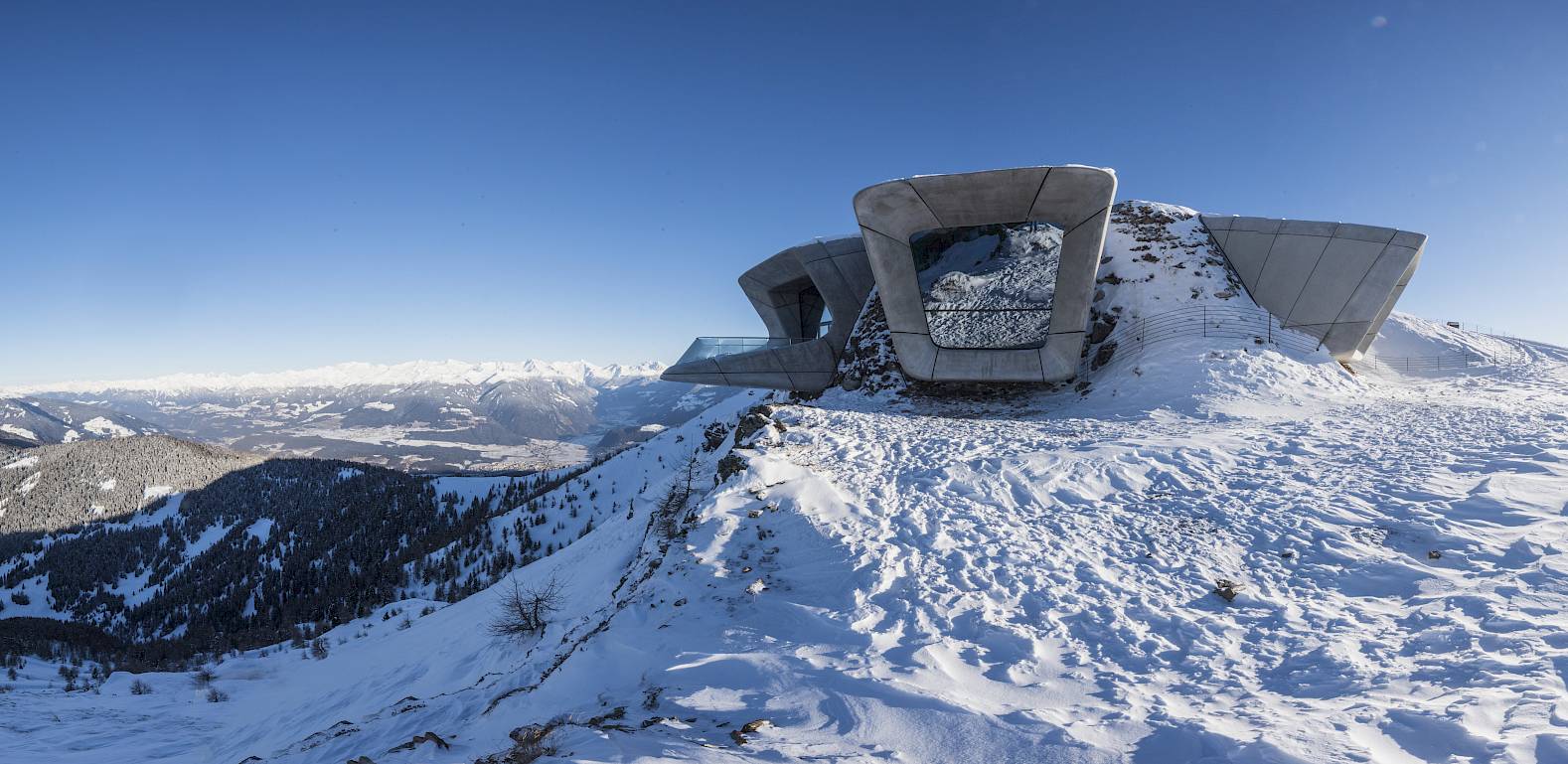 Modern, futuristic architecture on a snowy hill against a clear blue sky.