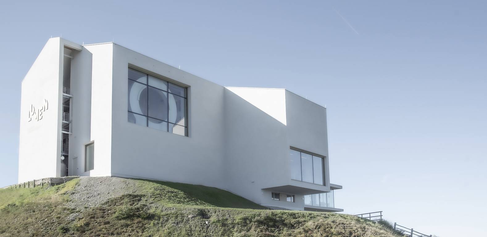 Modern white building on a hill, clear sky, with large windows and minimalist design.