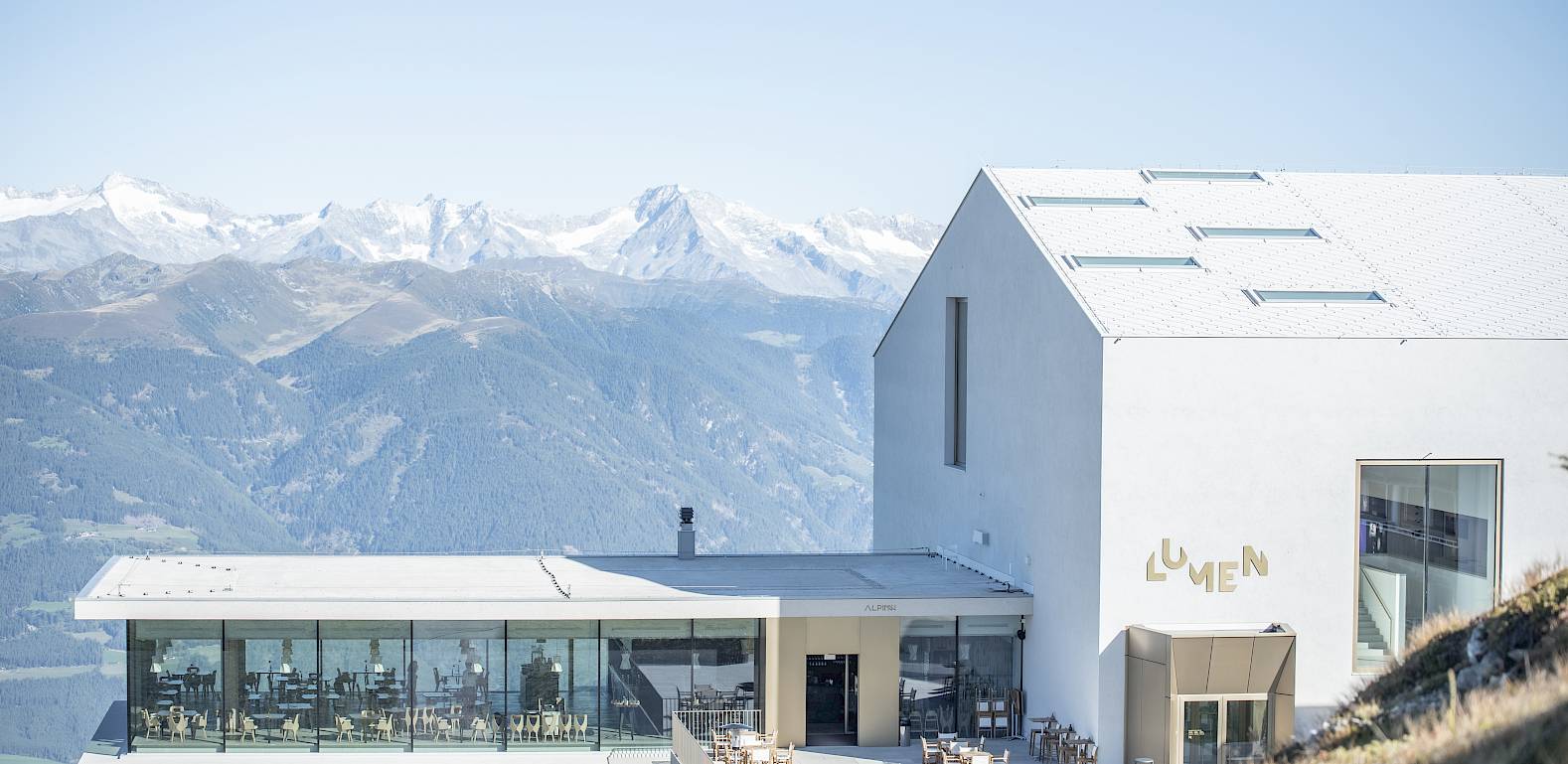 Modern building in a mountainous landscape, large windows and terrace with panoramic views of snowy peaks.