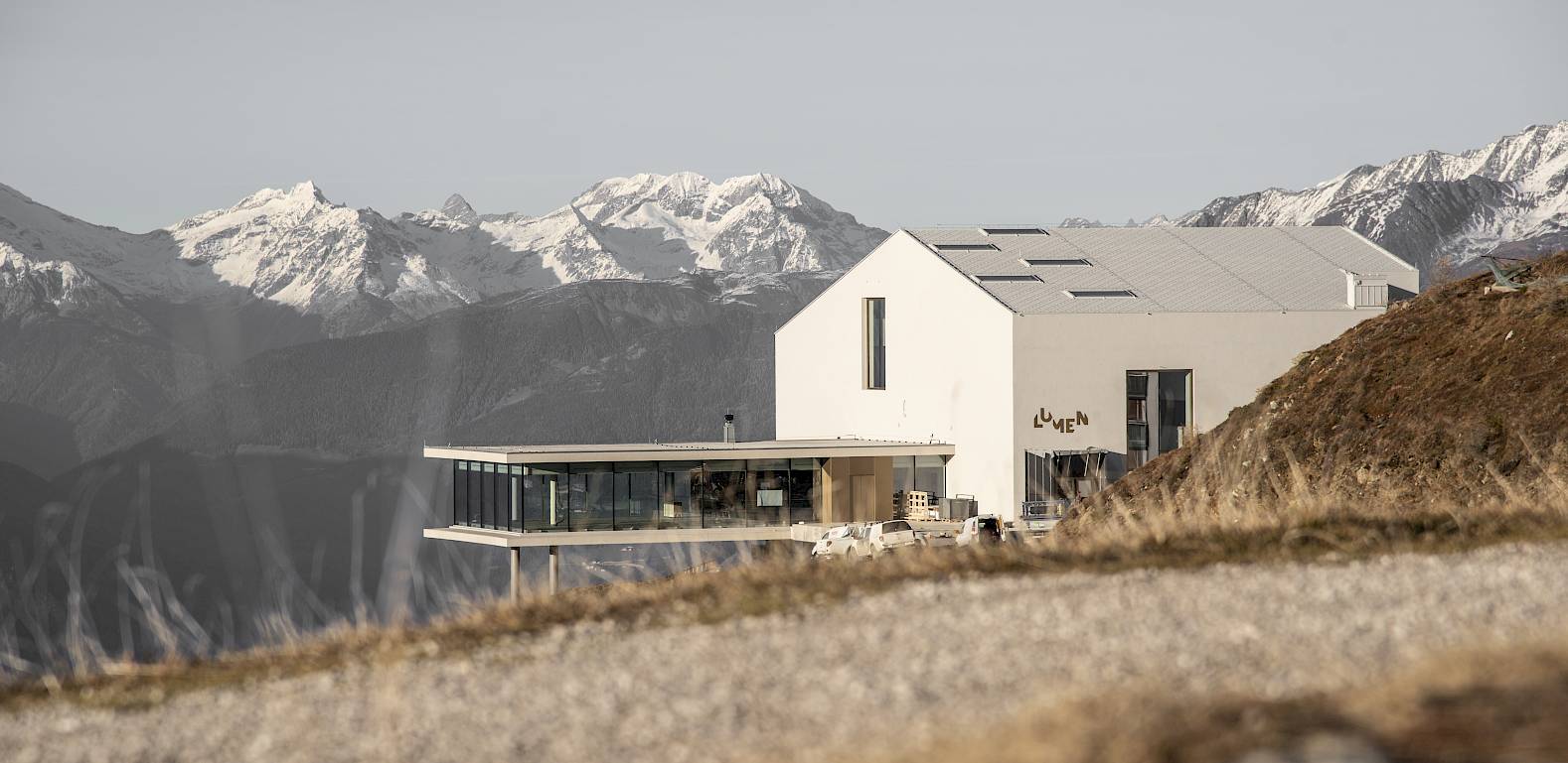 Modern building with large windows on a hill overlooking snow-covered Alps.