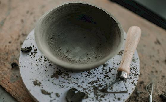 Ton-Schale in Arbeit auf Drehscheibe, umgeben von Tonresten und einem Holzwerkzeug.